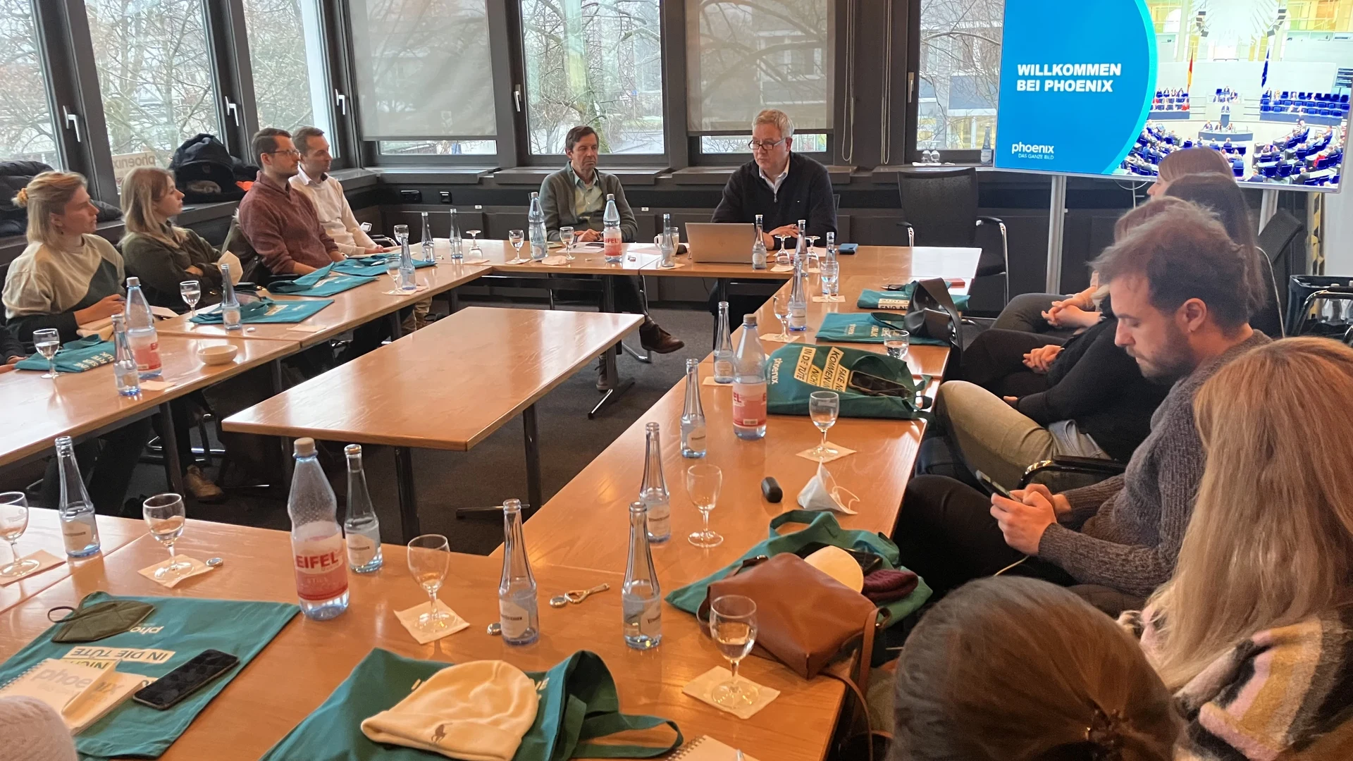 Eine Wissenschaftlerin und ein Wissenschaftler arbeiten hinter einer Glasfassade und mischen Chemikalien mit Großgeräten.