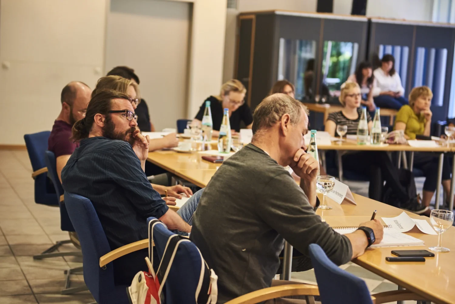 Eine Wissenschaftlerin und ein Wissenschaftler arbeiten hinter einer Glasfassade und mischen Chemikalien mit Großgeräten.